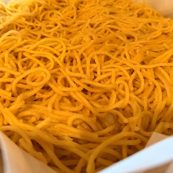 Close-up of a large serving of golden-yellow noodles, likely a side dish from Angry Chicken.