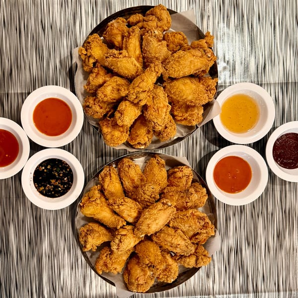 Two large platters of Angry Chicken's golden-brown fried chicken wings with various dipping sauces.