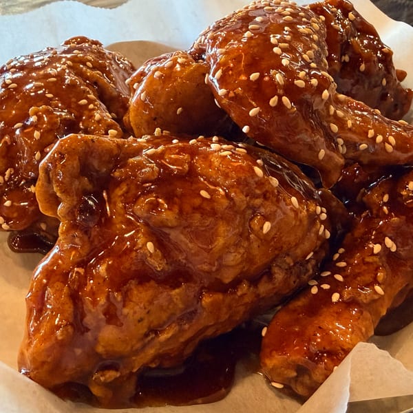 Close-up of Angry Chicken's fried chicken wings, coated in a glossy, dark sauce and sprinkled with sesame seeds.