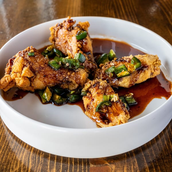 Angry Chicken's fried chicken pieces, glazed in a dark sauce and topped with sliced green peppers.