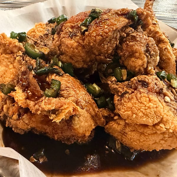 Crispy fried chicken pieces coated in a dark sauce and topped with chopped green peppers.