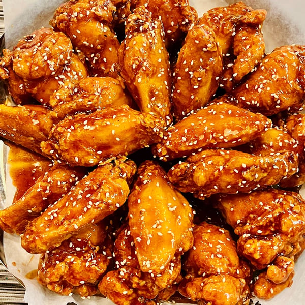Close-up of Angry Chicken's fried chicken wings, coated in a glossy sauce and sprinkled with sesame seeds.