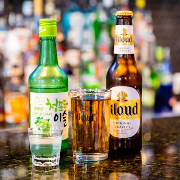 A green bottle of Jinro Green Grape Soju, a glass of beer, and a Kloud beer bottle.