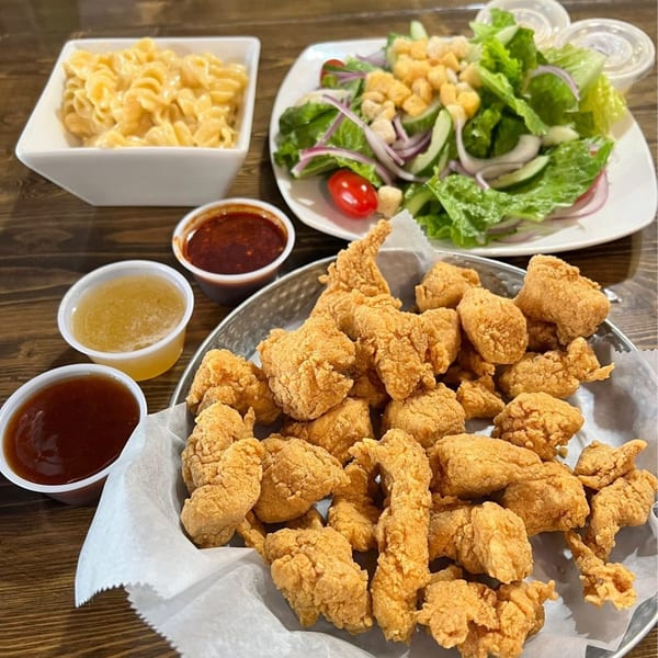Angry Chicken's fried chicken bites, mac and cheese, salad, and dipping sauces on a wooden table.