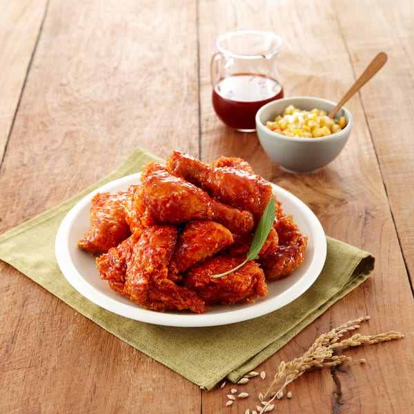Angry Chicken's spicy fried chicken on a white plate with corn and sauce on a wooden table.