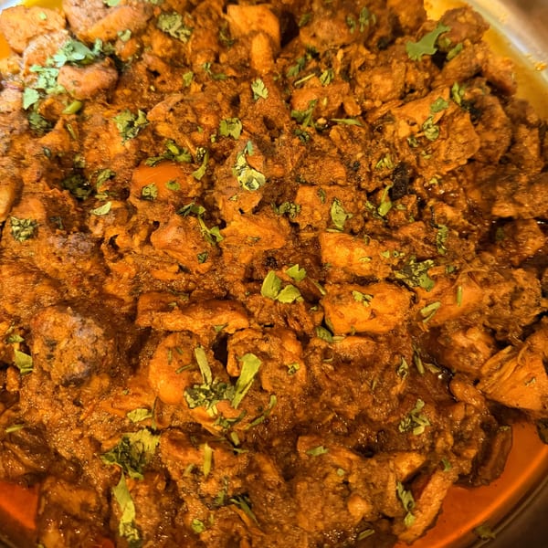 Close-up of Angry Chicken's fried chicken pieces coated in a rich, dark sauce and garnished with fresh cilantro.